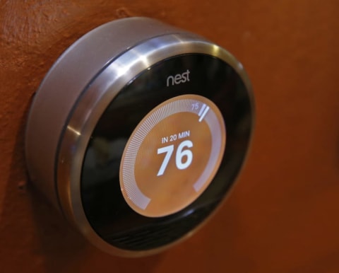 A circular thermostat that's silver on the outside with an electronic screen that shows the number 76 on an orange background.