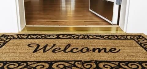 A welcome mat with a gold door threshold behind it.