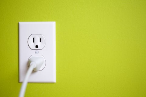 A white outlet with a cord plugged into it on a lime green wall.