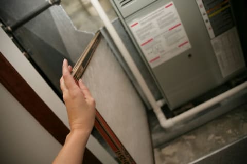 A hand putting a new furnace filter into a furnace.