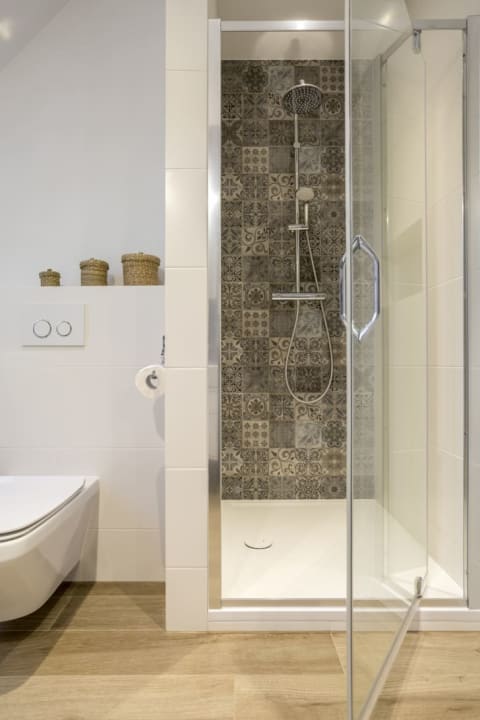 A clear shower door open to show the tiled wall inside. A white bathtub is off to the left.