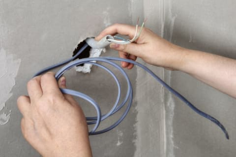 A hand is holding electrical work that has been pulled through a cement wall.