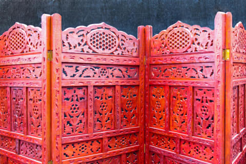 A red, wooden folding screen with intricate cut outs.