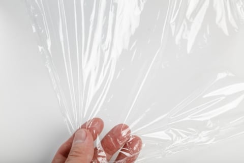 Fingers pulling on a sheet of clear plastic wrap.