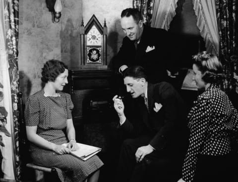 Four men and women gather closely together while listening to their home radio console, 1930s