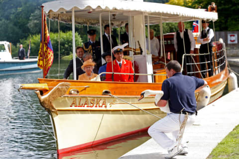 Queen Elizabeth II, accompanied by Swan Marker David Barber (red jacket), watches from the steam launch 'Alaska' as a swan upper places a swan back into the river during a swan upping census on the River Thames on July 20, 2009 near Windsor, England