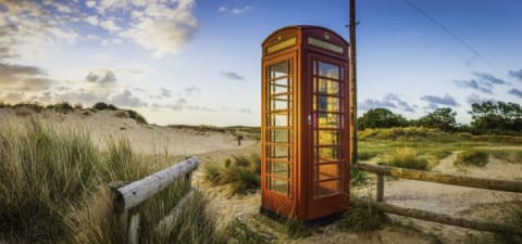 Red telephone box illuminated at sunrise on seaside beach in England