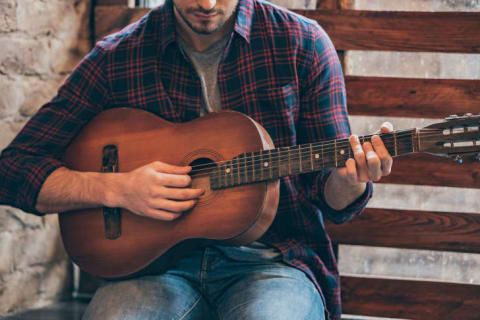 A man, shown from the nose down, playing a guitar.