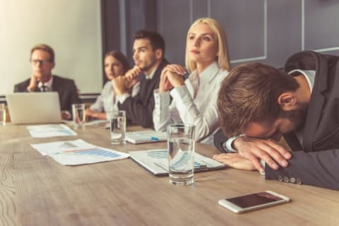 A man with his head on his arms, face down, during a meeting.