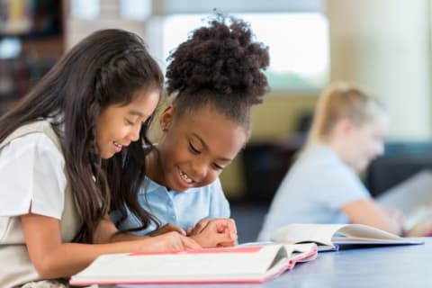 Two girls reading a book in the library.