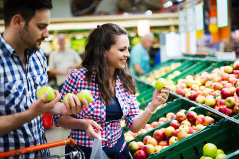 A man and woman looking at apples in the supermarket.