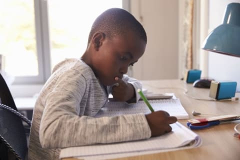 Young Boy In Bedroom Sitting At Desk Doing Homework