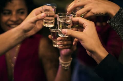 A group of people clinking full shot glasses together.