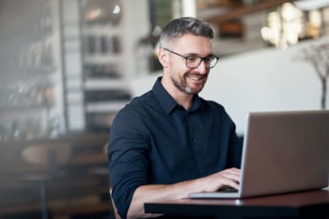 A man smiling while he types on his laptop.