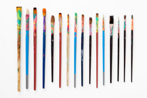 A bunch of dirty paint brushes on a white background.