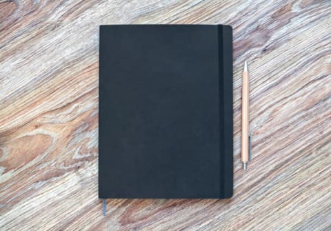 A planner on a wooden table with a pen next to it.