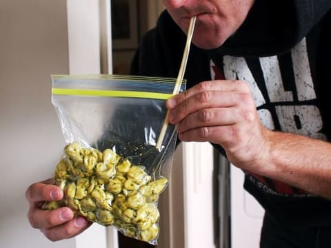 A man using a straw to suck the air out of a bag full of pasta.