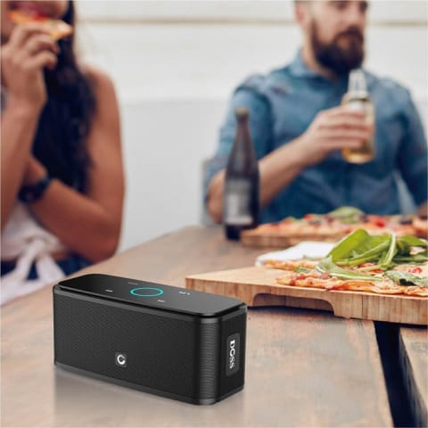 A portable speaker on a table with people eating pizza and drinking beer in the background