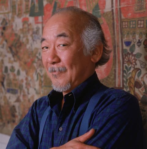 Portrait of actor Pat Morita standing against a tapestry, circa 1988.