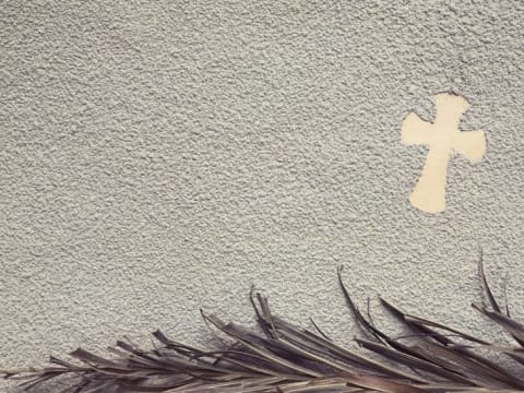 A cross and burned palm leaves in ash.