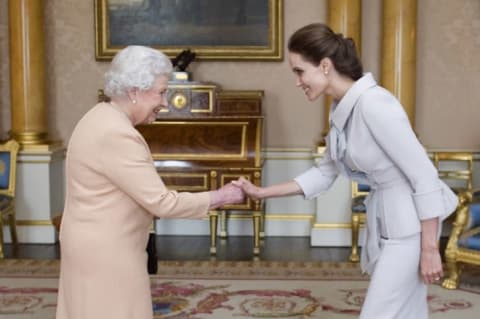 Queen Elizabeth II presents Angelina Jolie with the Insignia of an Honorary Dame Grand Cross of the Most Distinguished Order of St. Michael and St. George in 2014.