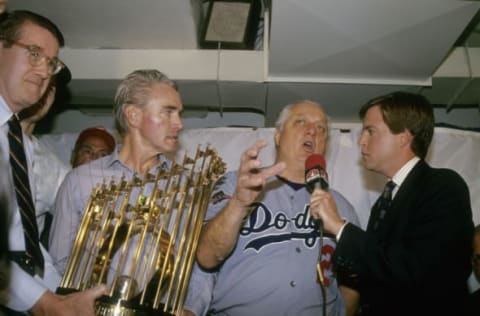 OAKLAND, CA – OCTOBER 20, 1988: Manager Tommy Lasorda #2 of the Los Angeles Dodgers in the Dodgers locker room, being interviewed by CBS sports broadcaster Bob Costas (R) while Dodgers owner Peter O’Malley, far left, holds the world series trophy after the Dodger beat the Oakland Athletics in game 5 to win the 1988 World Series, October 20, 1988 at the Oakland Coliseum in Oakland, California. The Dodgers won the series 4-1. Lasorda managed the Dodgers from 1976-1996. (Photo by Focus on Sport/Getty Images)