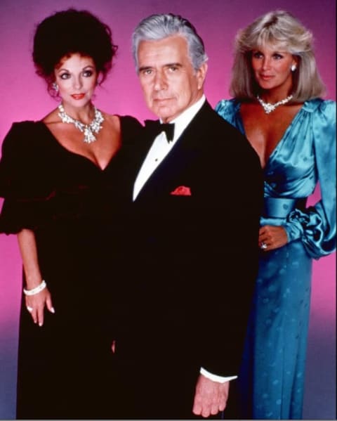 Joan Collins and Linda Evans compete for biggest shoulders with John Forsythe as judge in Dynasty.