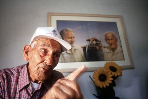 Gregorio Fuentes speaks in front of a photo of himself with Ernest Hemingway.