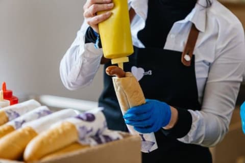 A person putting mustard in a Parek v Rohliku hot dog.