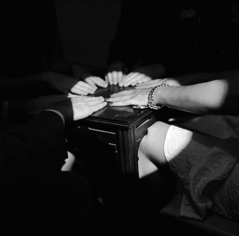 A medium uses her knee to tip a table during a seance.