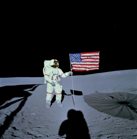 Alan Shepard, commander of the Apollo 14 lunar landing mission, stands on the moon. Shadows of the lunar module and astronaut Edgar D. Mitchell appear in the foreground.