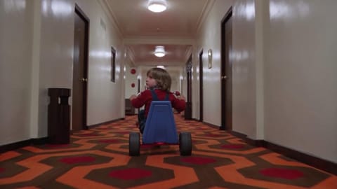 Danny pedals down the hallway of the eerie Overlook Hotel. 