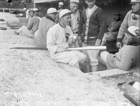 Informal three-quarter length portrait of baseball player Buck Weaver (1890 – 1956) of the American League’s Chicago White Sox, holding a silver baseball and a silver baseball bat, sitting on the ledge of a dugout at Comiskey Park, Chicago, Illinois, 1912. White Sox players are standing and sitting in the dugout in the background. (Photo by Chicago Sun-Times/Chicago Daily News collection/Chicago History Museum/Getty Images)