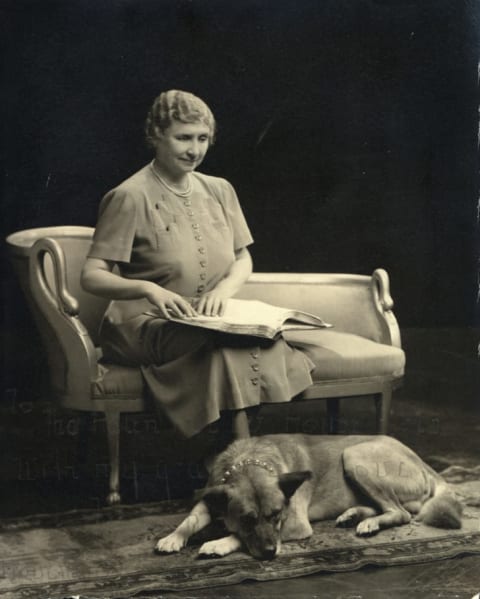 An Akita rests at Helen Keller's feet.