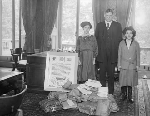 In 1918, Herbert Hoover was the director of the United States Food Administration, and was closely associated with relief efforts Europe. Here, he is standing with his wife and daughter by a poster giving thanks to America for its help in providing food.