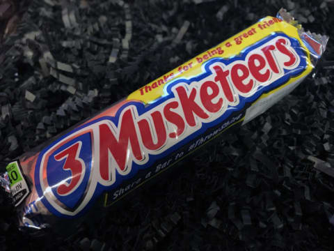 A 3 Musketeers bar on a black background.