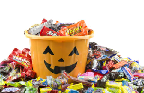 An orange pail with filled with, and surrounded by, Halloween candy.