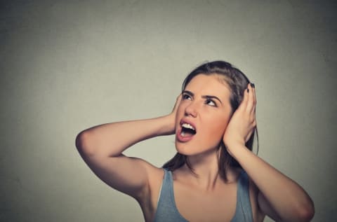 A woman with her hands over her ears, looking annoyed.