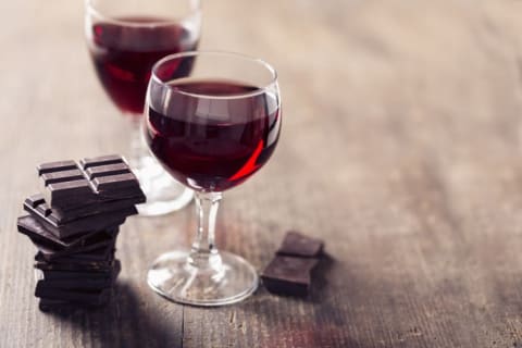 Two classes of red wine on a table with some chocolate.