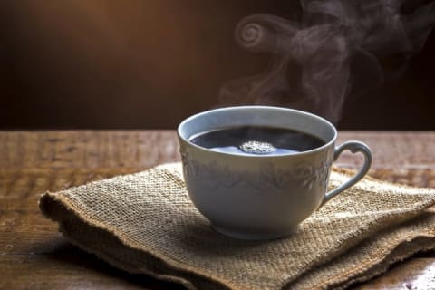 A steaming cup of coffee on a piece of burlap.