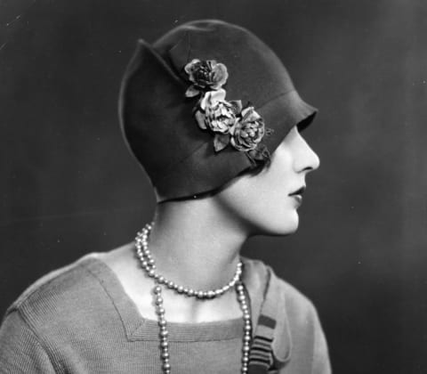 A woman wearing a cloche hat decorated with flowers.