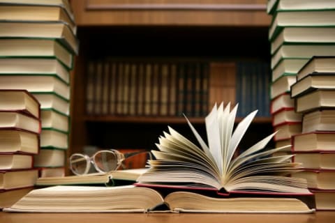 Stacks of books surrounding an open book and a pair of glasses.