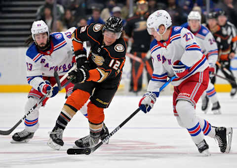 Jan 8, 2022; Anaheim, California, USA; Anaheim Ducks left wing Sonny Milano (12) and New York Rangers center Mika Zibanejad (93) and defenseman Nils Lundkvist (27) battle for the puck in the third period of the game at Honda Center. Mandatory Credit: Jayne Kamin-Oncea-USA TODAY Sports