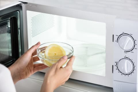 person putting a bowl and lemon in the microwave