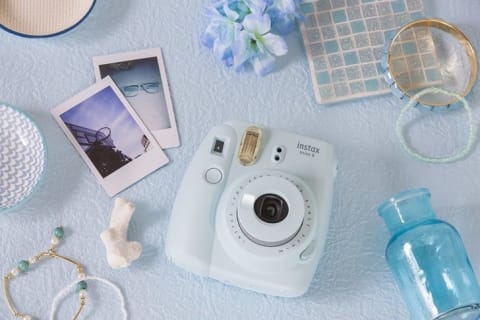 A Fujifilm instant camera on a table with several printed photos