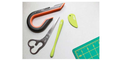 A box cutter, safety cutter, precision cutter, and scissors on a craft table