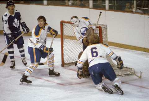 Professional hockey player Tim Horton of the Buffalo Sabres (#2) guards his net with fellow defenseman Jim Schoenfeld (#6) as Maple Leaf Paul Henderson (left) looks for a rebound, Buffalo, New York, early 1970s. The goalie for the Sabres is Roger Crozier. (Photo by Melchior DiGiacomo/Getty Images)