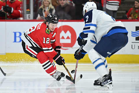 CHICAGO, ILLINOIS – MARCH 20: Alex DeBrincat #12 of the Chicago Blackhawks and Dylan Demelo #2 of the Winnipeg Jets battle for control of the puck in the second period on March 20, 2022 at the United Center in Chicago, Illinois. (Photo by Jamie Sabau/Getty Images)