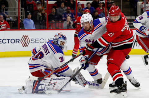 RALEIGH, NC – FEBRUARY 19: Nino Niederreiter #21 of the Carolina Hurricanes gets hit in the hip by a shot as he battles Tony DeAngelo #77 and goaltender Henrik Lundqvist #30 of the New York Rangers during an NHL game on February 19, 2019 at PNC Arena in Raleigh, North Carolina. (Photo by Karl DeBlaker/NHLI via Getty Images)