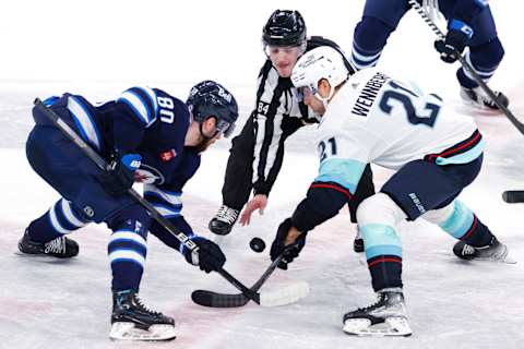 Feb 14, 2023; Winnipeg, Manitoba, CAN; Winnipeg Jets left wing Pierre-Luc Dubois (80) and Seattle Kraken center Alex Wennberg (21) face off in over time at Canada Life Centre. Mandatory Credit: James Carey Lauder-USA TODAY Sports